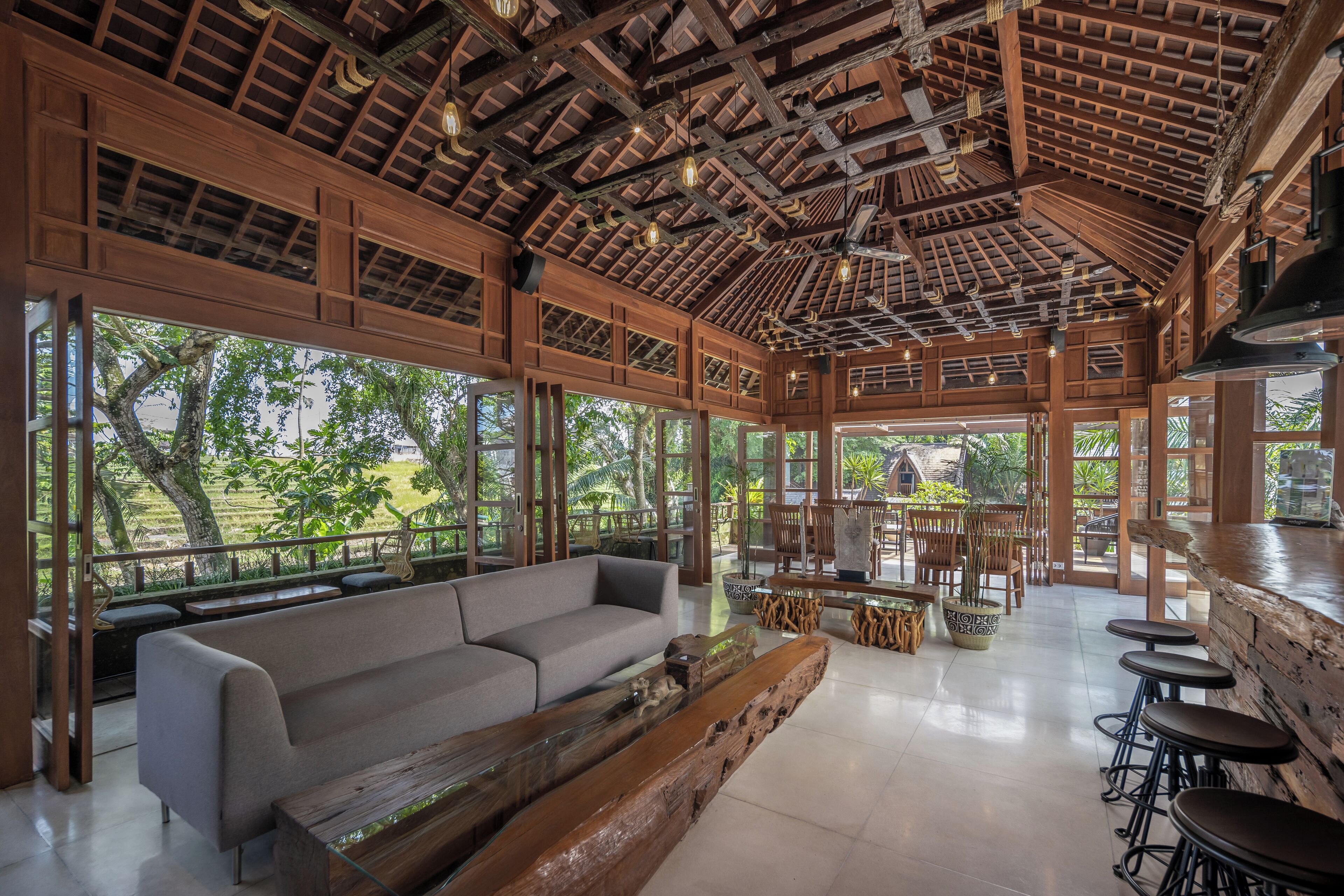 A spacious indoor area with a wooden ceiling, large windows, a sofa, and bar stools.