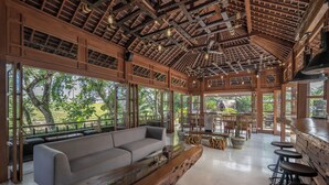 Un espace intérieur spacieux avec un plafond en bois, de grandes fenêtres, un canapé et des tabourets de bar.