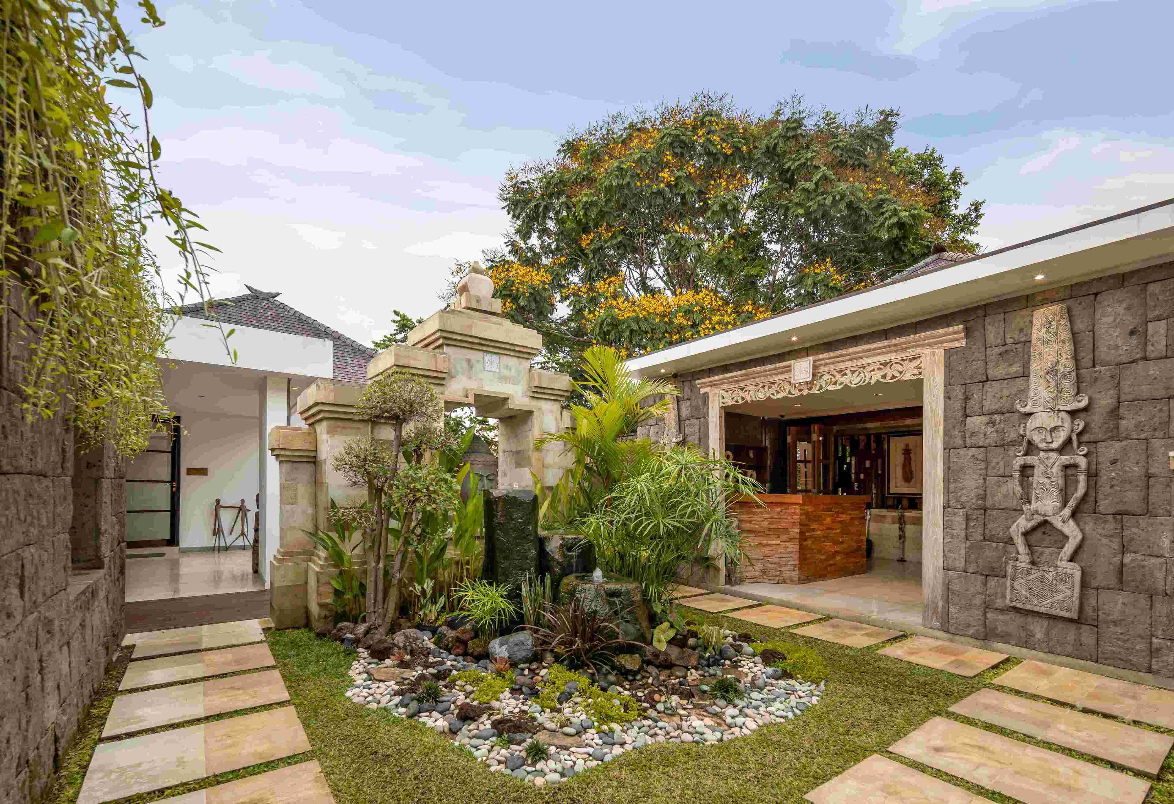 Un patio con un camino de piedra, un pequeño jardín con diversas plantas y un edificio de diseño tradicional.
