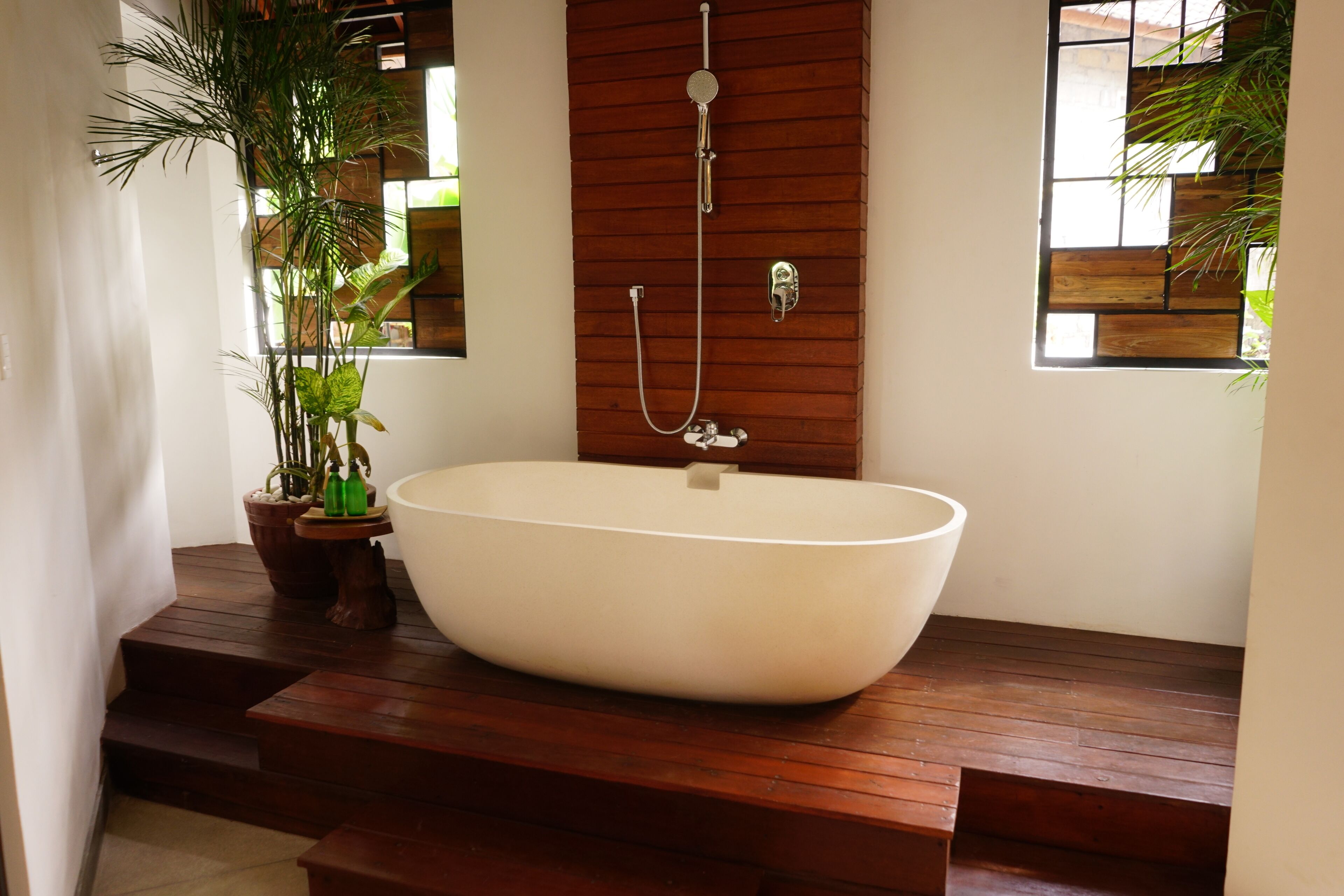 A modern bathroom with a freestanding bathtub, wooden steps, and potted plants.