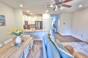 A modern kitchen with white cabinets, a stainless steel refrigerator, and a dining area with a wooden table and white chairs. - New Cozy SanDestin Beach TownHome/30A (Santa Rosa Beach)