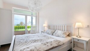 Een slaapkamer met een bed, twee bedlampen, een nachtkastje en uitzicht op een tuin door een glazen deur.