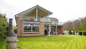 Een huis met twee verdiepingen, een balkon, een schoorsteen en een keurig onderhouden gazon.
