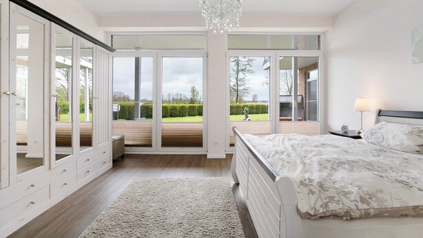 Een slaapkamer met een bed, een kroonluchter, een nachtkastje, een lamp en grote glazen deuren die uitkomen op een terras.