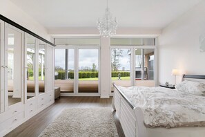 Quarto com cama, candelabro, mesa de cabeceira, abajur e grandes portas de vidro que dão para uma área externa.