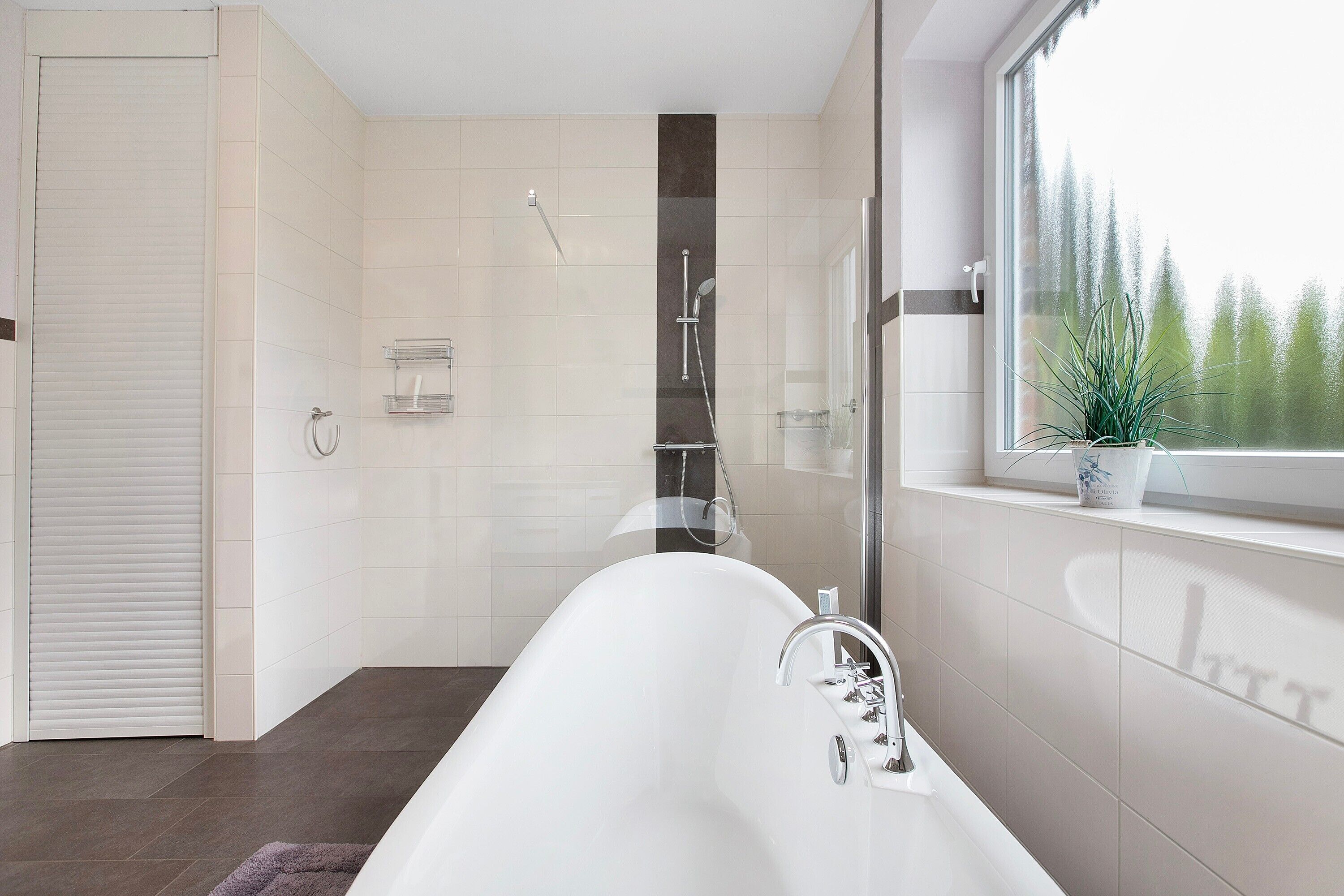 Een moderne badkamer met een vrijstaand bad, een douche en een raam met uitzicht op bomen.