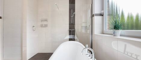 Een moderne badkamer met een vrijstaand bad, een douche en een raam met uitzicht op bomen.