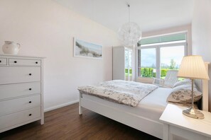 Quarto com cama, cômoda, luminária, janela com vista e luminária pendente.