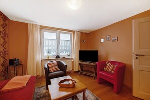A living room with a sofa, a red armchair, a television, and a window with curtains. - Holiday Home 'Haus Gertrud' with Mountain View, Private Terrace and Wi-Fi (Monzelfeld)