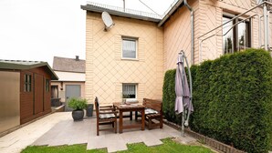 A residential building with a patio, a wooden table and chairs, a potted plant, and a hedge. - Holiday Home 'Haus Gertrud' with Mountain View, Private Terrace and Wi-Fi (Monzelfeld)