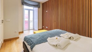 A modern hotel room with a large bed, a wooden panel wall, and a balcony view. - Vita Portucale Setubal Deluxe Apartment (Setúbal)