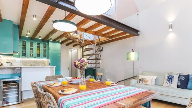 A modern kitchen with wooden beams, a dining area with a wooden table, wicker chairs, and a striped tablecloth. - Vita Portucale Setubal Deluxe Apartment (Setúbal)