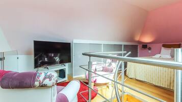 A compact hotel room with a bed, a TV, a chair, and a small table.