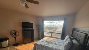 Ein Schlafzimmer mit Bett, Fernseher, Ventilator und Fenster mit Außenblick.