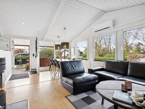 A modern living room with a black leather sofa, a dining area with a table and chairs, and large windows offering a view of the outdoors. - "Safina" - 100m from the sea by Interhome (Broager)