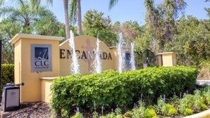 Une enseigne pour « EMANCIPADA », avec un logo, entourée d’une végétation luxuriante et de palmiers.