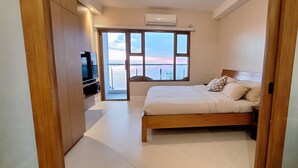 Een slaapkamer met een bed, een televisie en een groot raam met uitzicht op zee.