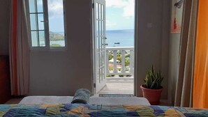A bedroom with a bed, a window, a balcony, and a potted plant. - Atlantic Breeze Apartments  (Canouan Island)
