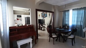 A dining area with a round table and chairs, a wooden bench, and a kitchen in the background. - Atlantic Breeze Apartments  (Canouan Island)