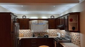 A compact kitchen with dark wooden cabinets, a tiled backsplash, and a gas stove. - Atlantic Breeze Apartments  (Canouan Island)