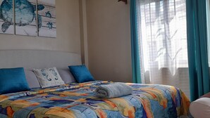 A bed with a colorful quilt, a pillow with a sea turtle design, and a wall with a sea turtle artwork. - Atlantic Breeze Apartments  (Canouan Island)