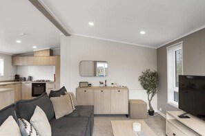 A modern living room with a sofa, a coffee table, a TV, and a kitchen area with wooden cabinets and a countertop.