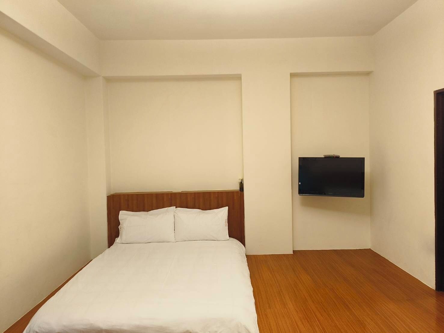 A hotel room with a wooden headboard, a bed with white bedding, and a flat-screen TV mounted on the wall.
