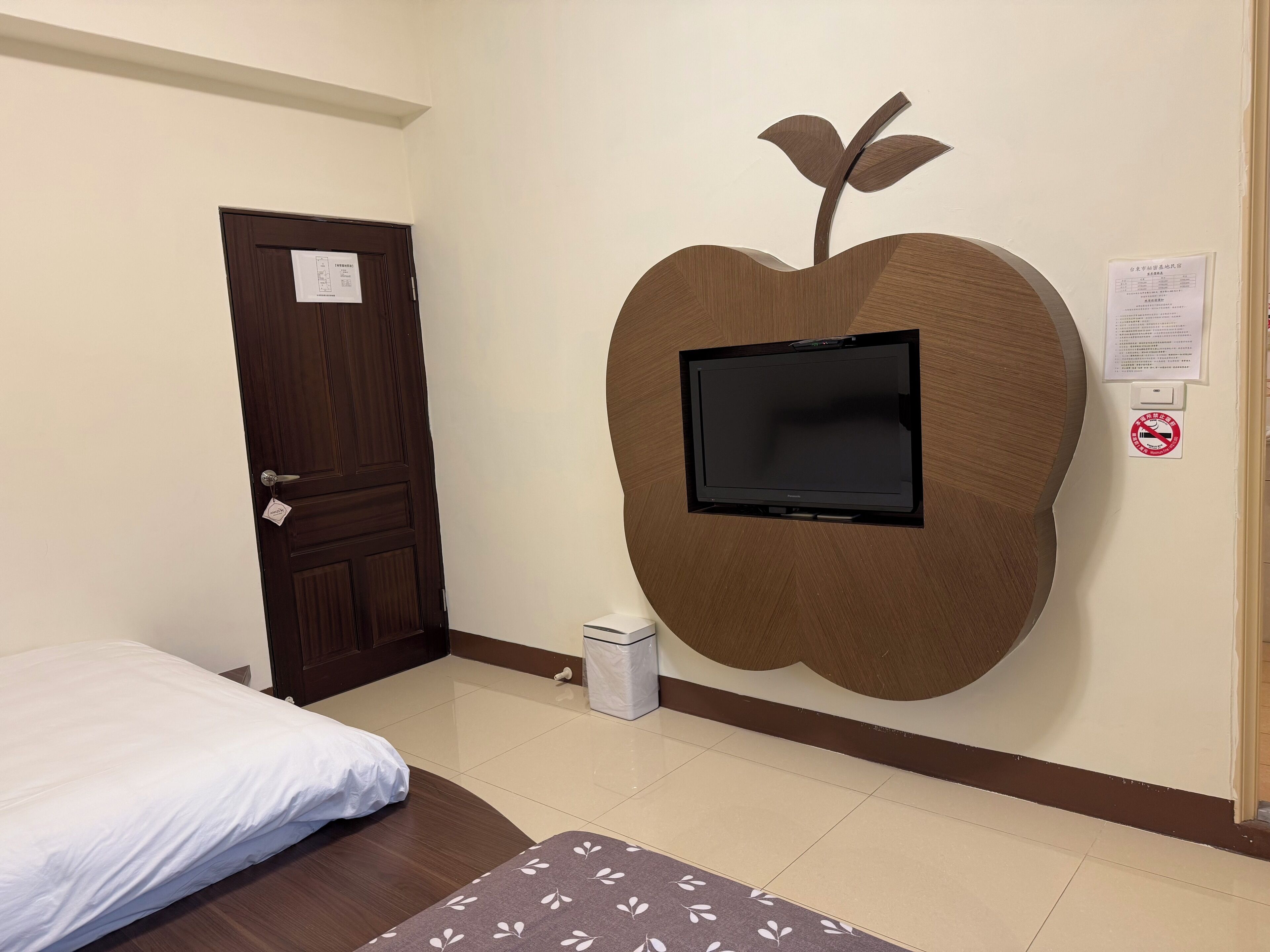 Una habitación de hotel con cama, televisor montado en la pared y una puerta con un cartel.