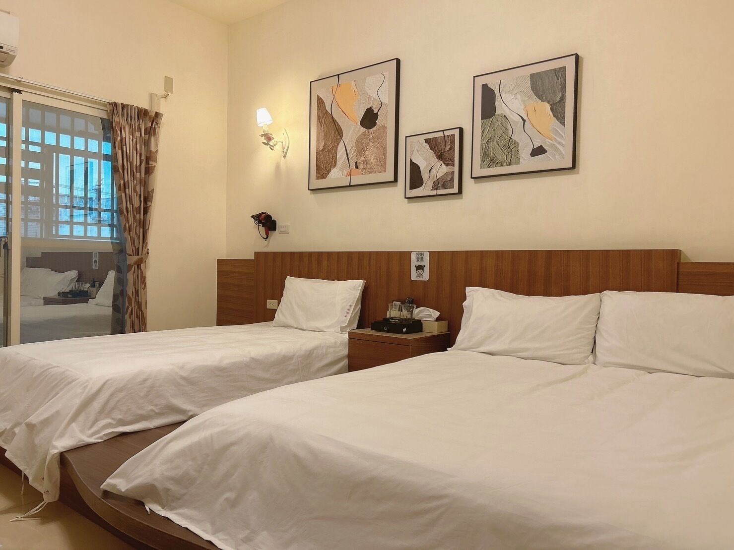 Una habitación de hotel con dos camas, un cabecero de madera, una mesita de noche y arte abstracto en la pared.