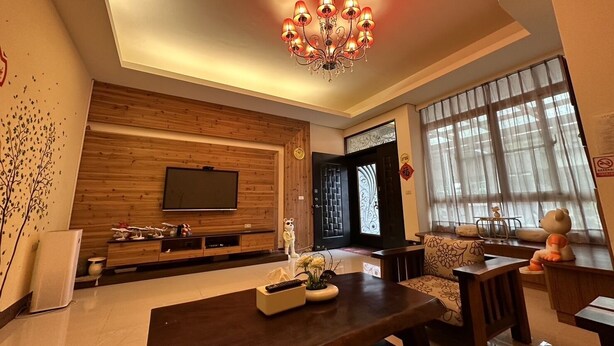 A modern living room with a wooden wall unit, a TV, a dining table with chairs, and a decorative chandelier. - Secret base B&B (Taitung)