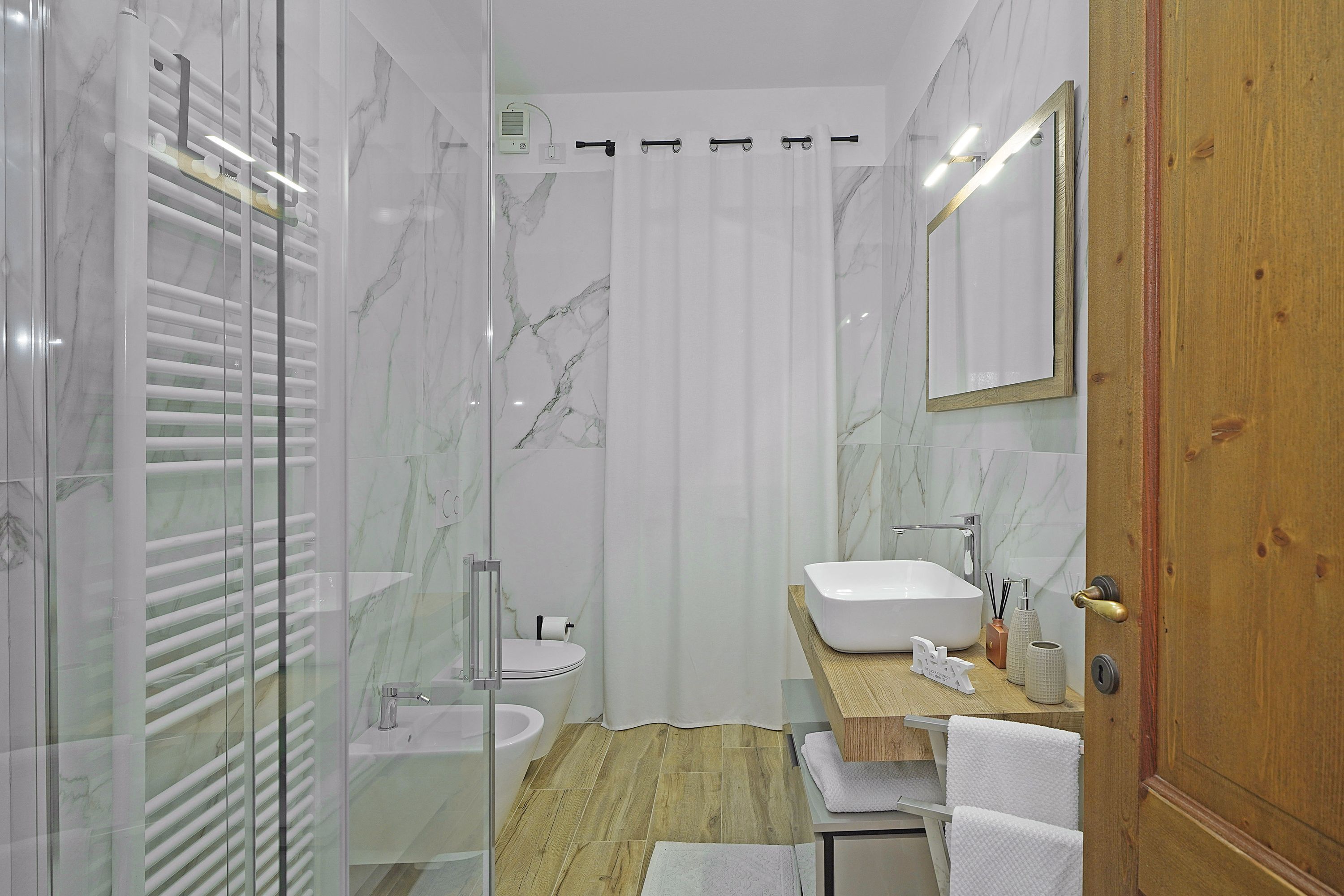 Ein modernes Badezimmer mit Duschkabine aus Glas, einem Holzbadezimmermöbel, einem weißen Waschbecken und einem Spiegel.