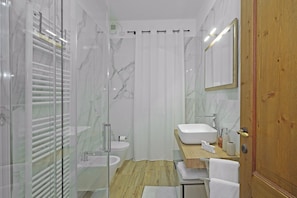 A modern bathroom with a glass shower enclosure, a wooden vanity, a white sink, and a mirror.