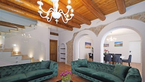 Ein großzügiger Wohnbereich mit zwei grünen Sofas, einer Glasstiege und einem Essbereich im Hintergrund.