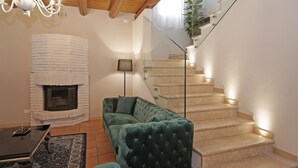 Ein Wohnzimmer mit Kamin, einem grünen Sofa, einer Glastreppe und einem Chandelier.