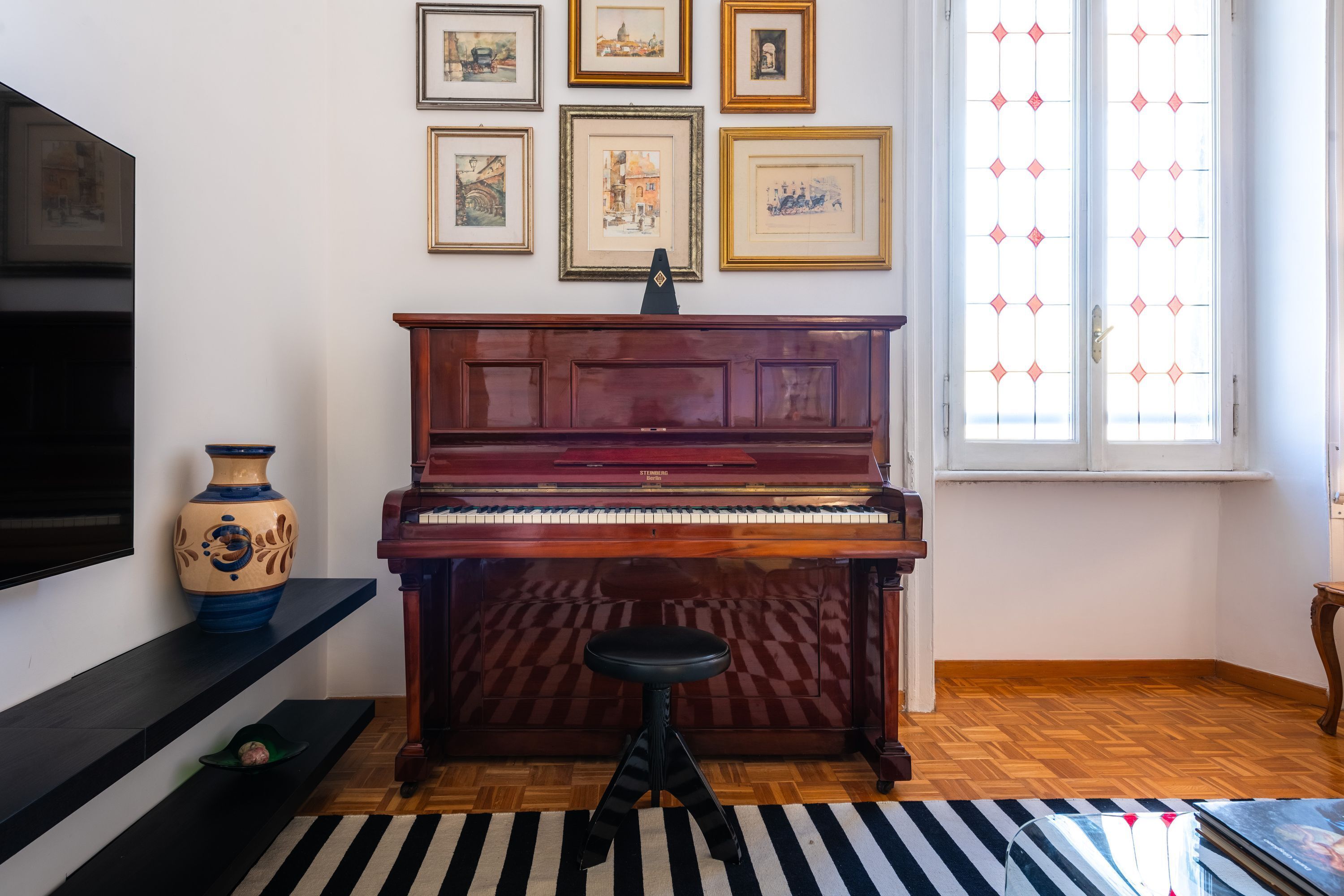 A room with a piano, a television, a vase, and framed pictures on the wall.