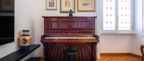 A room with a piano, a television, a vase, and framed pictures on the wall.