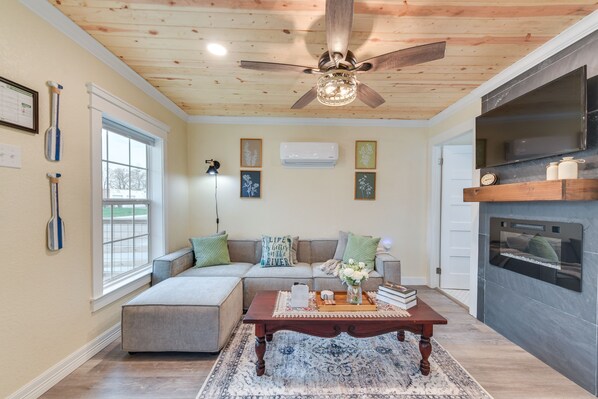 A cozy living room with a wooden ceiling, a ceiling fan, a fireplace, a sofa, and a coffee table with decorative items.