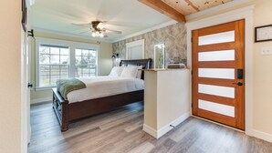 Ein Schlafzimmer mit Bett, Holzbalkendecke, einer Tür mit Frostglas-Elementen und einem Fenster mit Blick ins Freie.