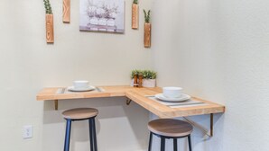 Ein Eckzimmer mit einem Holztisch, zwei Hocker, einem Gemälde und hängenden Pflanzgefäßen aus Holz.