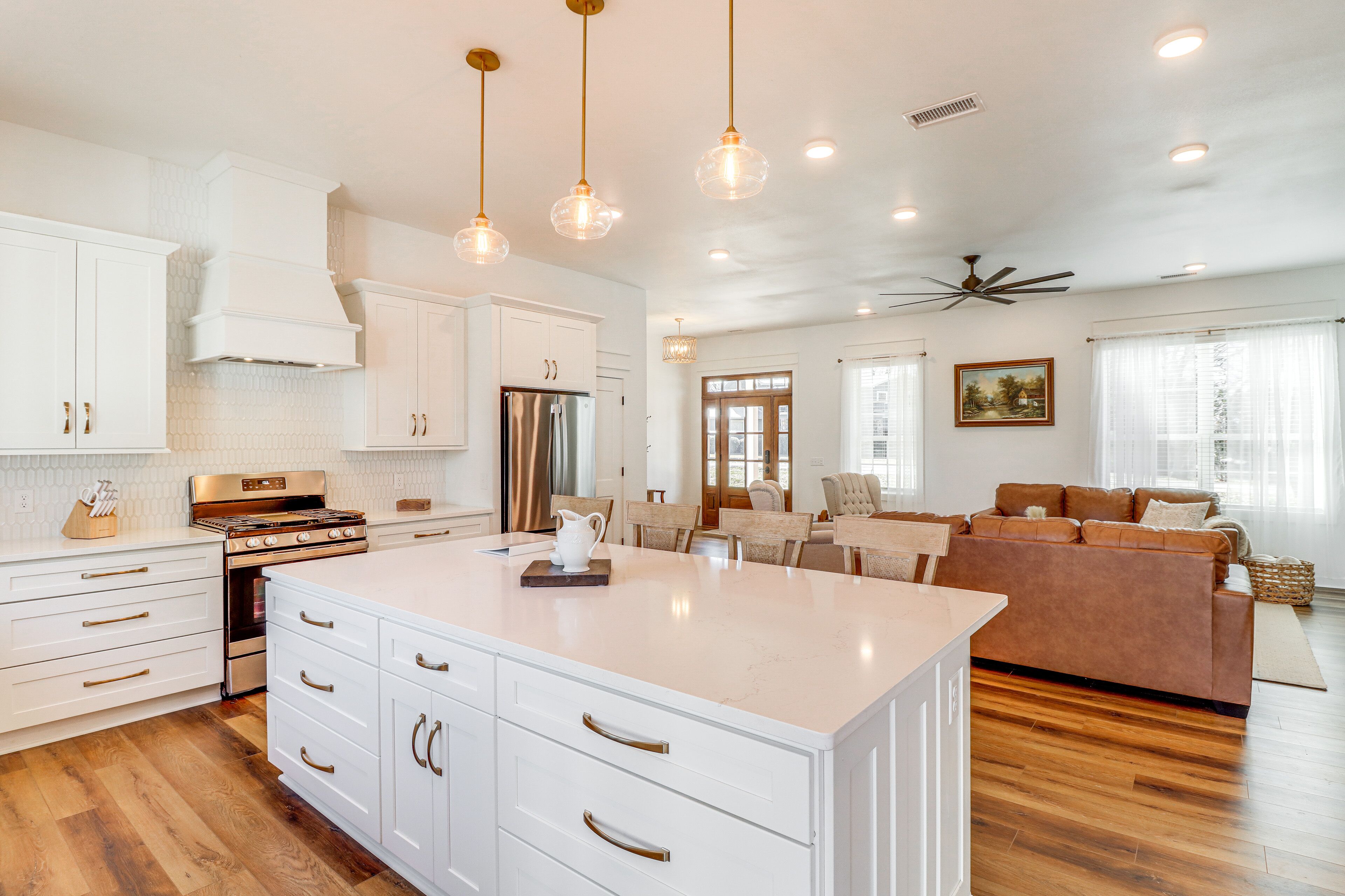 A spacious kitchen with white cabinetry, a large island, and a dining area with a brown leather couch.