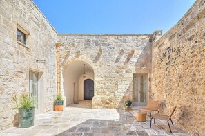 A stone courtyard with an arched entrance, potted plants, and wicker furniture. - Villa Tindaro: A modern and graceful two-story villa with the fascination of the typical courtyard houses of Salento area, with Free WI-FI. (Surano)