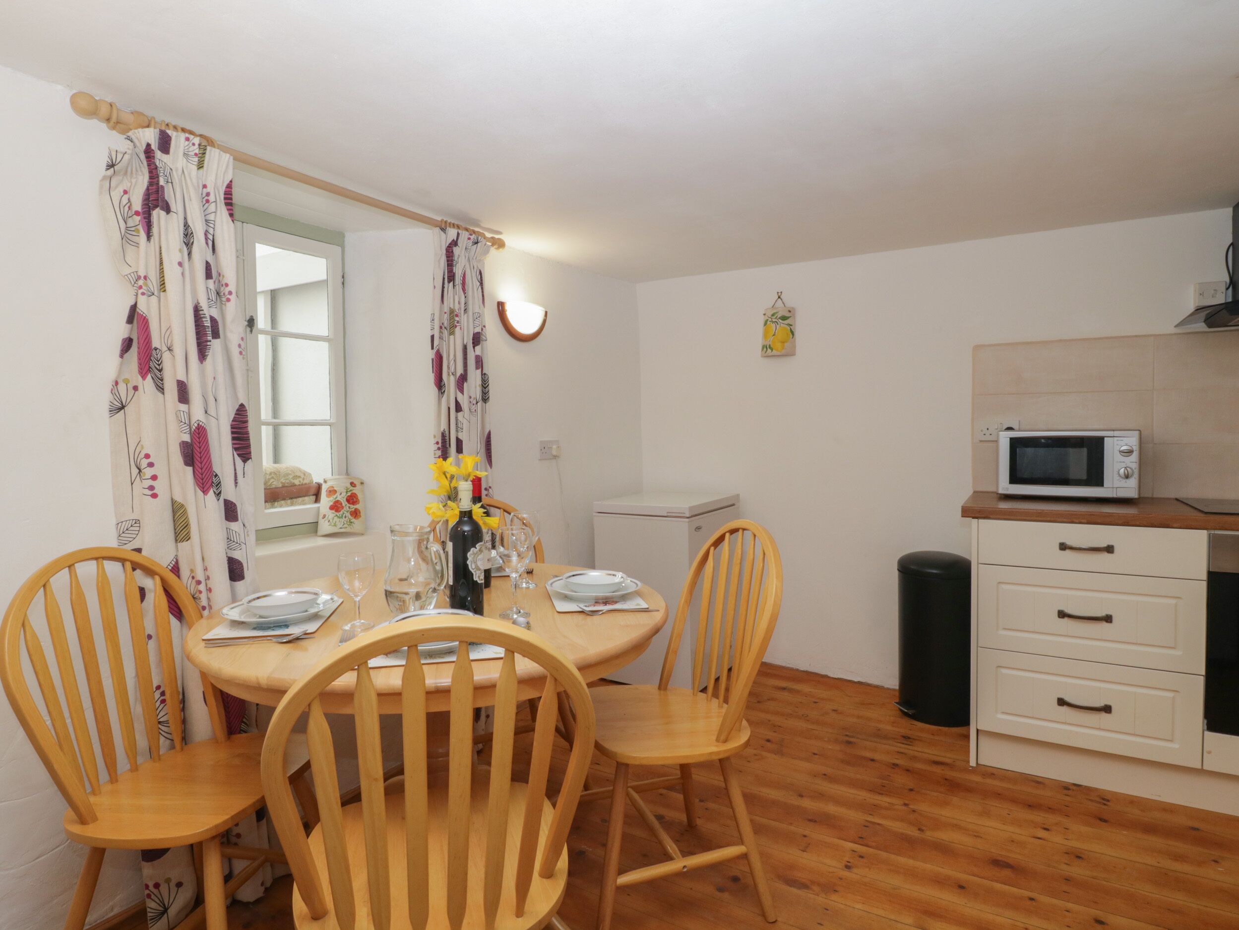 Une petite cuisine accueillante, avec des chaises en bois, une table à manger dressée pour deux personnes et un four à micro-ondes posé sur le plan de travail.