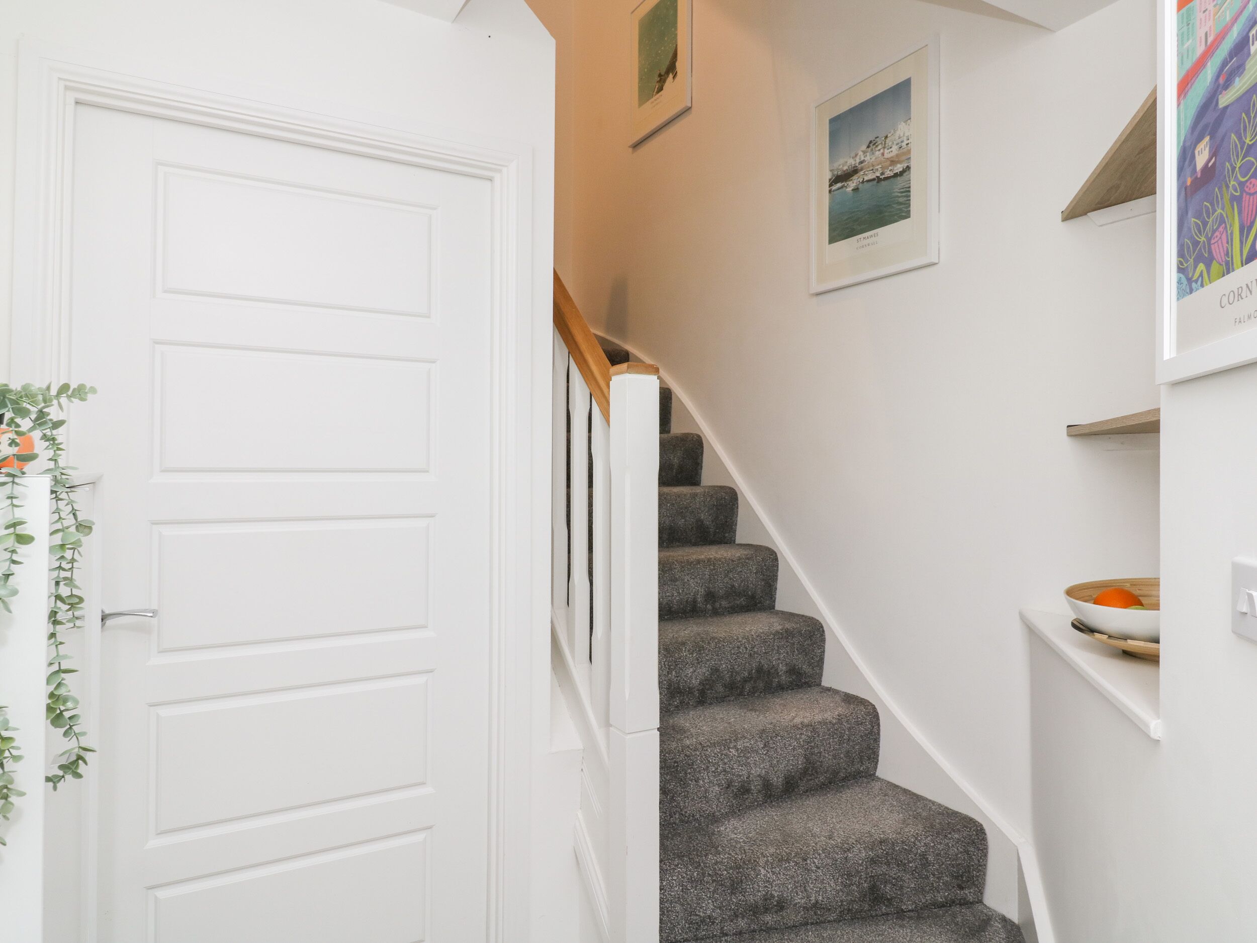 Un escalier avec des marches recouvertes d’une moquette grise, des murs blancs et une porte blanche.