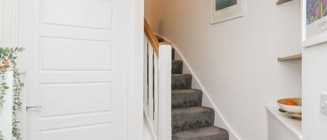 Un escalier avec des marches recouvertes d’une moquette grise, des murs blancs et une porte blanche.
