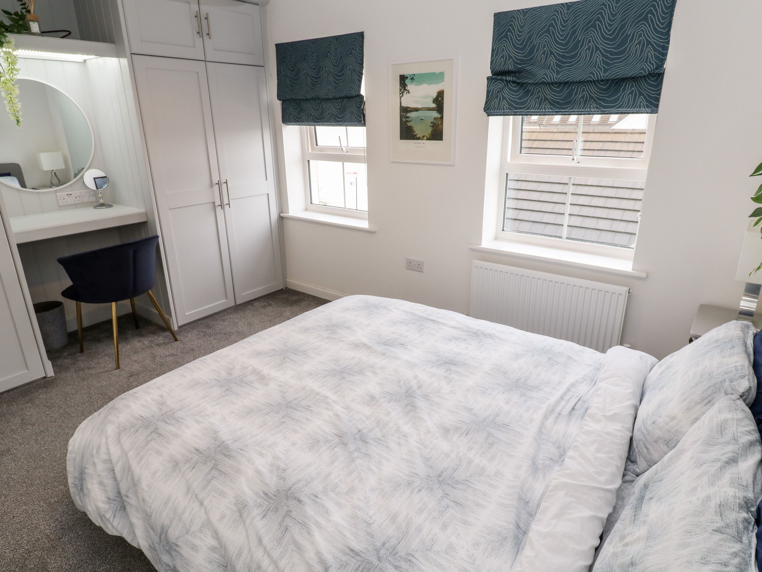 A bedroom with a bed, a desk, and a chair. There is a window with a view of the outside.