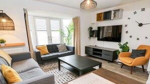Een moderne woonkamer met een bank, fauteuils, een salontafel en een televisie.