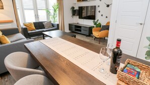 Een moderne woonkamer met een houten eettafel, grijze banken en een flatscreen televisie.