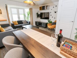 A modern living room with a wooden dining table, grey sofas, and a flat-screen TV.