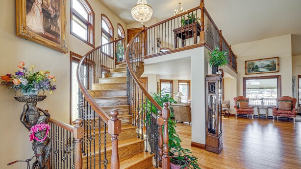A spacious living area with a wooden staircase, large windows, and a chandelier.