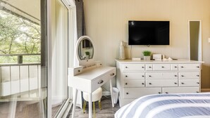 A bedroom with a white dresser, a vanity with a mirror, a flat-screen TV mounted above the dresser, and a bed with striped bedding.
